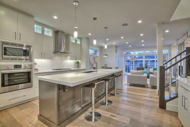 Inspiration for a large contemporary l-shaped medium tone wood floor kitchen remodel in Calgary with an undermount sink, flat-panel cabinets, white cabinets, quartz countertops, white backsplash, stainless steel appliances and an island