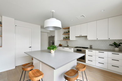 Mid-sized trendy l-shaped medium tone wood floor and beige floor open concept kitchen photo in New York with an undermount sink, flat-panel cabinets, white cabinets, quartz countertops, gray backsplash, ceramic backsplash, stainless steel appliances and an island
