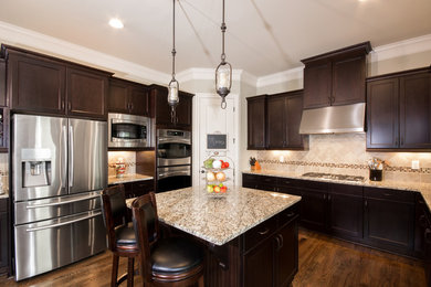 Example of a mid-sized classic u-shaped medium tone wood floor open concept kitchen design in Atlanta with a double-bowl sink, shaker cabinets, dark wood cabinets, granite countertops, beige backsplash, mosaic tile backsplash, stainless steel appliances and an island