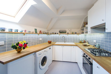 Inspiration for a small contemporary u-shaped kitchen/diner in London with a belfast sink, flat-panel cabinets, white cabinets, wood worktops, blue splashback, cement tile splashback, white appliances and lino flooring.