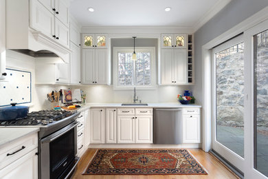 Example of a mid-sized classic l-shaped medium tone wood floor enclosed kitchen design in New York with an undermount sink, raised-panel cabinets, white cabinets, quartz countertops, white backsplash, subway tile backsplash, stainless steel appliances and no island