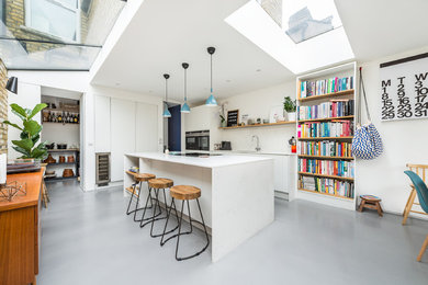 Medium sized contemporary kitchen/diner in London with an integrated sink, flat-panel cabinets, white cabinets, quartz worktops, white splashback, brick splashback, stainless steel appliances, concrete flooring, an island and grey floors.