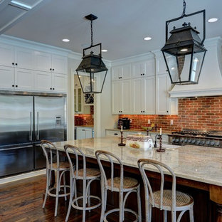 Farmhouse kitchen ideas - Country l-shaped dark wood floor and brown floor kitchen photo in Atlanta with a farmhouse sink, shaker cabinets, white cabinets, granite countertops, brick backsplash, stainless steel appliances, an island, red backsplash and gray countertops