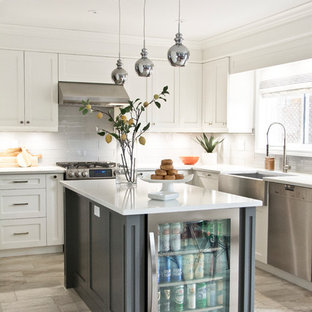 Modelo de cocina en L, tradicional renovada, con fregadero sobremueble, armarios estilo shaker, puertas de armario blancas, salpicadero verde, salpicadero de azulejos de vidrio, electrodomésticos de acero inoxidable, una isla y suelo gris