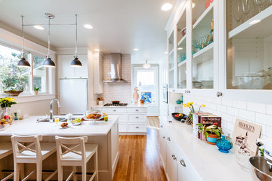 Klassische Küche mit Doppelwaschbecken, Glasfronten, weißen Schränken, Küchenrückwand in Weiß, Rückwand aus Metrofliesen, weißen Elektrogeräten, hellem Holzboden und Halbinsel in Portland