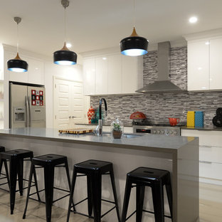 Photo of a mid-sized l-shaped kitchen in Other with a drop-in sink, flat-panel cabinets, white cabinets, multi-coloured splashback, mosaic tile splashback, stainless steel appliances, ceramic floors, beige floor, with island and grey benchtop.