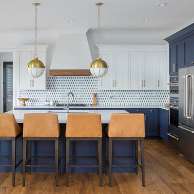 Beach style l-shaped medium tone wood floor and brown floor kitchen photo in Indianapolis with an undermount sink, shaker cabinets, blue cabinets, multicolored backsplash, stainless steel appliances, an island and white countertops
