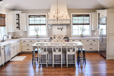 Inspiration for a farmhouse u-shaped medium tone wood floor kitchen remodel in New Orleans with a farmhouse sink, raised-panel cabinets, gray cabinets, gray backsplash, stainless steel appliances and an island
