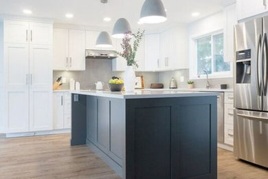 Example of a large arts and crafts l-shaped laminate floor and brown floor open concept kitchen design in Vancouver with an undermount sink, shaker cabinets, gray cabinets, quartz countertops, gray backsplash, porcelain backsplash, stainless steel appliances, an island and white countertops