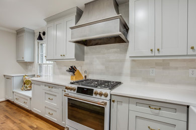 Example of a mid-sized transitional u-shaped medium tone wood floor and brown floor enclosed kitchen design in Birmingham with a farmhouse sink, recessed-panel cabinets, gray cabinets, quartz countertops, white backsplash, marble backsplash, white appliances, an island and white countertops