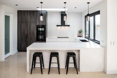 Inspiration for a medium sized contemporary u-shaped kitchen/diner in Melbourne with a submerged sink, flat-panel cabinets, white cabinets, engineered stone countertops, white splashback, ceramic splashback, black appliances, concrete flooring, no island, white worktops and beige floors.