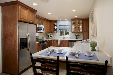 Elegant ceramic tile eat-in kitchen photo in Phoenix with an undermount sink, raised-panel cabinets, medium tone wood cabinets, solid surface countertops, white backsplash, ceramic backsplash and stainless steel appliances