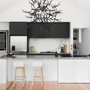 This is an example of a mid-sized contemporary galley open plan kitchen in Melbourne with an integrated sink, flat-panel cabinets, black cabinets, stainless steel benchtops, white splashback, stainless steel appliances, medium hardwood floors, a peninsula, marble splashback, brown floor and white benchtop.