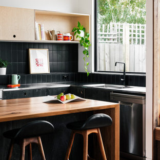 Inspiration for a contemporary l-shaped kitchen in Melbourne with an integrated sink, flat-panel cabinets, black cabinets, stainless steel benchtops, black splashback, stainless steel appliances, with island and grey benchtop.