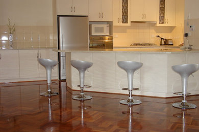 Cette image montre une cuisine ouverte minimaliste en U de taille moyenne avec un placard à porte plane, des portes de placard blanches, une crédence blanche, une crédence en céramique, un électroménager blanc et un sol en bois brun.