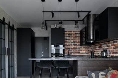 На фото: п-образная кухня-гостиная среднего размера в стиле лофт с плоскими фасадами, черными фасадами, коричневым фартуком, фартуком из кирпича, черной техникой, полуостровом, серым полом и черной столешницей