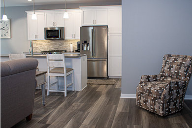 Open concept kitchen - contemporary single-wall vinyl floor and gray floor open concept kitchen idea in Other with shaker cabinets, white cabinets, gray backsplash, ceramic backsplash, stainless steel appliances and an island