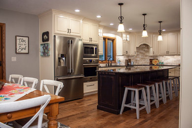 Example of a transitional u-shaped light wood floor eat-in kitchen design in Other with white cabinets, granite countertops, beige backsplash, stone tile backsplash, stainless steel appliances, an island and black countertops