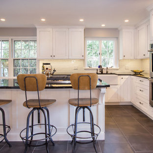 Photo of a medium sized farmhouse l-shaped kitchen/diner in Philadelphia with a belfast sink, shaker cabinets, white cabinets, granite worktops, white splashback, metro tiled splashback, stainless steel appliances, porcelain flooring and an island.
