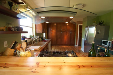 Moderne Küche in L-Form mit Vorratsschrank, Doppelwaschbecken, profilierten Schrankfronten, dunklen Holzschränken, Arbeitsplatte aus Fliesen, Küchengeräten aus Edelstahl und braunem Holzboden in Sonstige