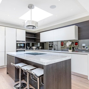 This is an example of a contemporary l-shaped kitchen/diner in London with a submerged sink, flat-panel cabinets, white cabinets, mirror splashback, light hardwood flooring and an island.