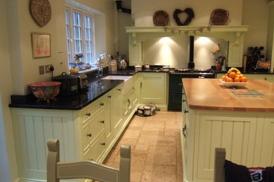Medium sized traditional u-shaped kitchen/diner in London with a belfast sink, shaker cabinets, green cabinets, granite worktops, black splashback, limestone flooring and an island.