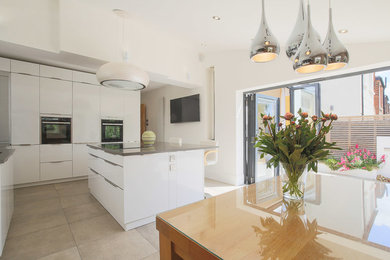 Photo of a large modern u-shaped open plan kitchen in London with flat-panel cabinets, white cabinets, an island and beige floors.