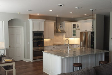 Example of a large classic l-shaped dark wood floor and brown floor open concept kitchen design in Jacksonville with a farmhouse sink, shaker cabinets, white cabinets, quartzite countertops, white backsplash, subway tile backsplash, stainless steel appliances, an island and multicolored countertops