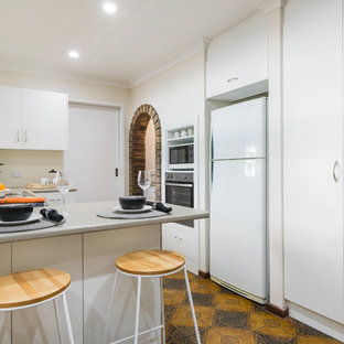 Small contemporary u-shaped kitchen in Perth with flat-panel cabinets, white cabinets, beige splashback, white appliances, a peninsula, orange floor and grey benchtop.