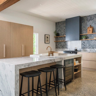 Design ideas for a country l-shaped kitchen in Sydney with a drop-in sink, flat-panel cabinets, light wood cabinets, grey splashback, black appliances, concrete floors, with island, beige floor and grey benchtop.