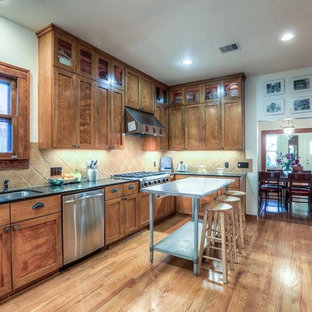 Idées déco pour une grand arrière-cuisine craftsman en U avec un évier encastré, un placard à porte shaker, des portes de placard en bois brun, un plan de travail en surface solide, une crédence beige, une crédence en carrelage de pierre, un électroménager en acier inoxydable, un sol en bois brun et un îlot central.