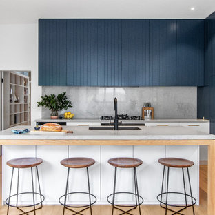 This is an example of a contemporary galley kitchen in Sydney with an undermount sink, blue cabinets, with island, grey benchtop, marble benchtops, multi-coloured splashback, marble splashback, black appliances and light hardwood floors.