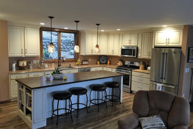 Inspiration for a mid-sized rustic l-shaped laminate floor and brown floor open concept kitchen remodel in Other with an undermount sink, raised-panel cabinets, white cabinets, laminate countertops, stainless steel appliances and an island