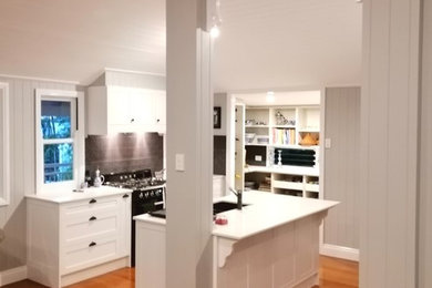 Klassische Küche mit Unterbauwaschbecken, Schrankfronten im Shaker-Stil, weißen Schränken, Quarzwerkstein-Arbeitsplatte, Küchenrückwand in Grau, Rückwand aus Keramikfliesen, braunem Holzboden, Kücheninsel und weißer Arbeitsplatte in Brisbane