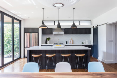 Inspiration for a contemporary galley medium tone wood floor and brown floor eat-in kitchen remodel in San Francisco with an undermount sink, flat-panel cabinets, black cabinets, white backsplash, stainless steel appliances, an island and white countertops