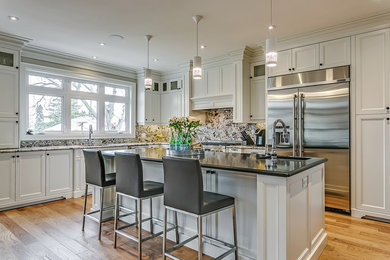 Mid-sized elegant l-shaped light wood floor open concept kitchen photo in Toronto with an undermount sink, recessed-panel cabinets, white cabinets, stainless steel appliances, an island, granite countertops, beige backsplash and stone slab backsplash