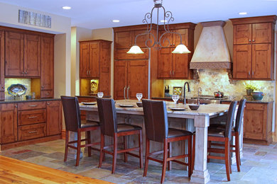 Example of a large mountain style galley slate floor eat-in kitchen design in Milwaukee with a farmhouse sink, recessed-panel cabinets, medium tone wood cabinets, granite countertops, multicolored backsplash, stone tile backsplash, paneled appliances and an island
