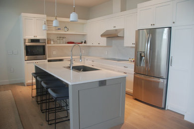 バンクーバーにあるコンテンポラリースタイルのおしゃれなキッチン (白いキャビネット、珪岩カウンター、石スラブのキッチンパネル、シルバーの調理設備) の写真