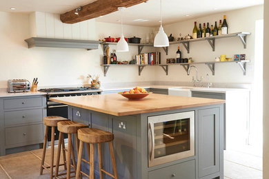 Inspiration for a farmhouse l-shaped kitchen in Other with a belfast sink, shaker cabinets, grey cabinets, black appliances, an island and grey floors.