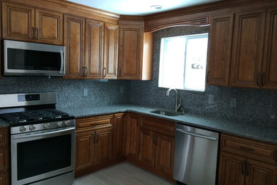 Example of a mid-sized classic l-shaped porcelain tile and brown floor kitchen design in Philadelphia with an undermount sink, raised-panel cabinets, medium tone wood cabinets, blue backsplash, stone slab backsplash and stainless steel appliances