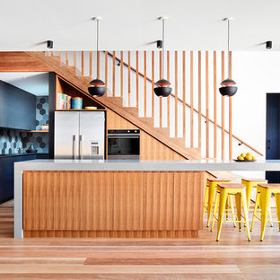 Inspiration for a mid-sized contemporary l-shaped open plan kitchen in Melbourne with flat-panel cabinets, solid surface benchtops, porcelain splashback, stainless steel appliances, medium hardwood floors, with island, brown floor, grey cabinets, multi-coloured splashback and grey benchtop.