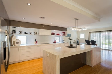 Foto de cocina minimalista grande con fregadero encastrado, puertas de armario blancas, salpicadero blanco, electrodomésticos negros, suelo de bambú y una isla