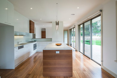 Foto på ett stort funkis kök, med en köksö, vitt stänkskydd, glaspanel som stänkskydd, rostfria vitvaror, en dubbel diskho och ljust trägolv