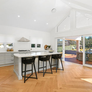 Design ideas for an expansive country l-shaped open plan kitchen in Wollongong with a farmhouse sink, shaker cabinets, grey cabinets, quartz benchtops, white splashback, ceramic splashback, stainless steel appliances, with island, medium hardwood floors, brown floor and white benchtop.
