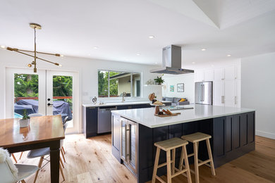 Example of a mid-sized trendy single-wall light wood floor and brown floor open concept kitchen design in Vancouver with an undermount sink, shaker cabinets, blue cabinets, quartz countertops, white backsplash, stone slab backsplash, stainless steel appliances, an island and white countertops