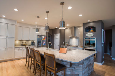 Example of a large eclectic single-wall light wood floor and beige floor open concept kitchen design in Denver with an undermount sink, raised-panel cabinets, white cabinets, quartz countertops, beige backsplash, glass tile backsplash, stainless steel appliances and an island