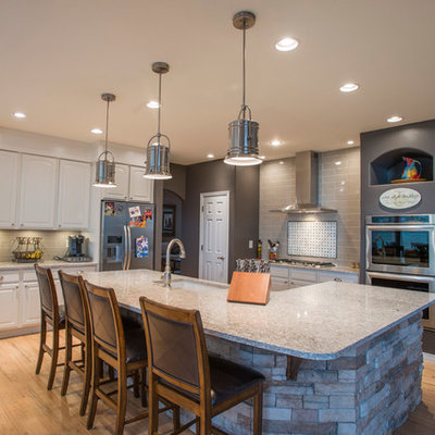 Example of a large eclectic single-wall light wood floor and beige floor open concept kitchen design in Denver with an undermount sink, raised-panel cabinets, white cabinets, quartz countertops, beige backsplash, glass tile backsplash, stainless steel appliances and an island