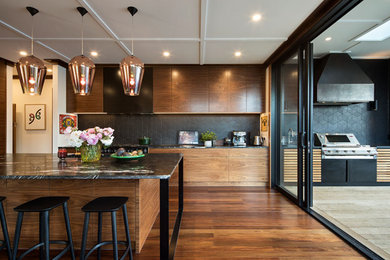Inspiration for a large retro l-shaped kitchen/diner in Auckland with a double-bowl sink, raised-panel cabinets, medium wood cabinets, granite worktops, black splashback, ceramic splashback, black appliances, an island and black worktops.