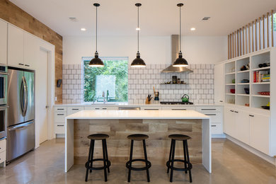 Inspiration for a mid-sized country u-shaped concrete floor open concept kitchen remodel in Austin with an undermount sink, flat-panel cabinets, white cabinets, white backsplash, stainless steel appliances, an island, solid surface countertops, porcelain backsplash and white countertops