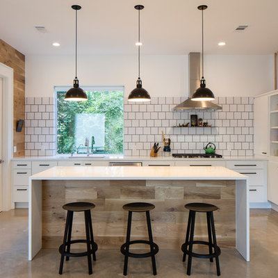 Inspiration for a mid-sized country u-shaped concrete floor open concept kitchen remodel in Austin with an undermount sink, flat-panel cabinets, white cabinets, white backsplash, stainless steel appliances, an island, solid surface countertops, porcelain backsplash and white countertops
